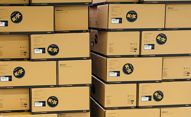 Gestapelte Kartons mit BOOMSTER AC/DC Edition Lautsprechern, bereit für den Versand von der Druckerei Union-Klischee.